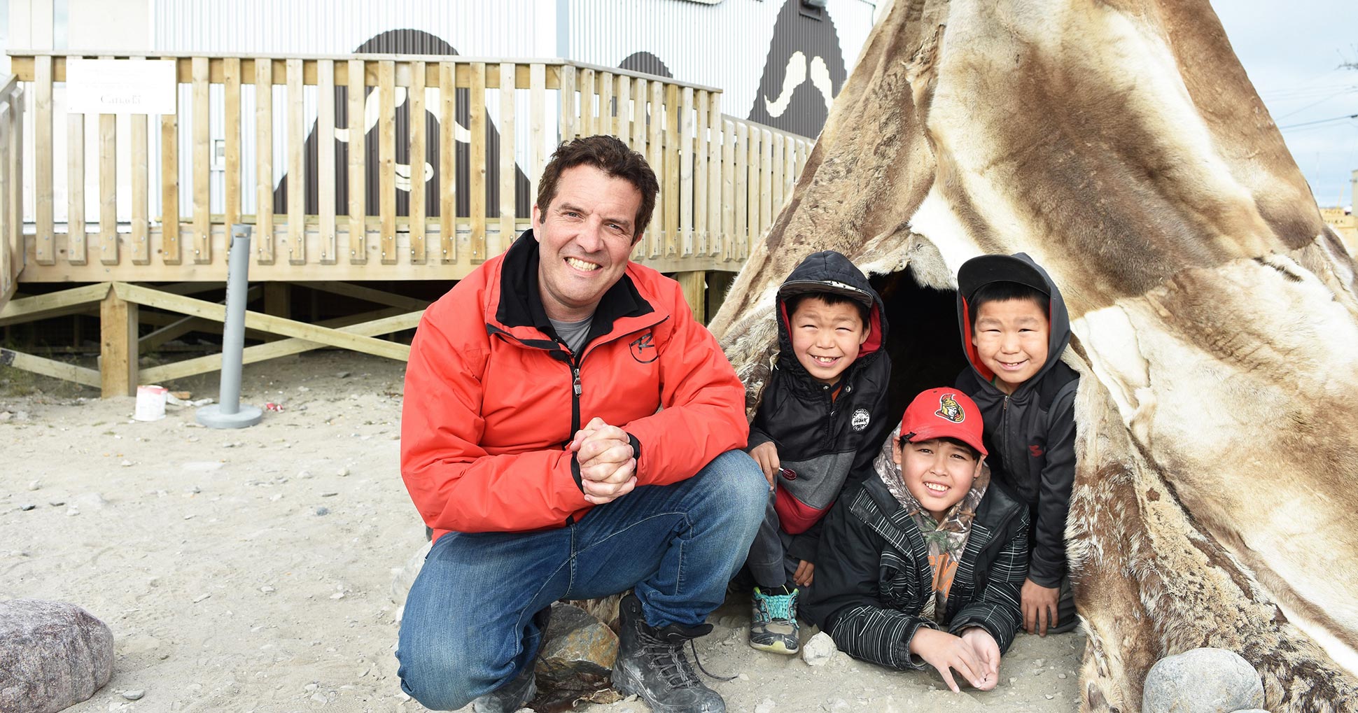 Rick Mercer sourit à côté de trois enfants du Nunavut.